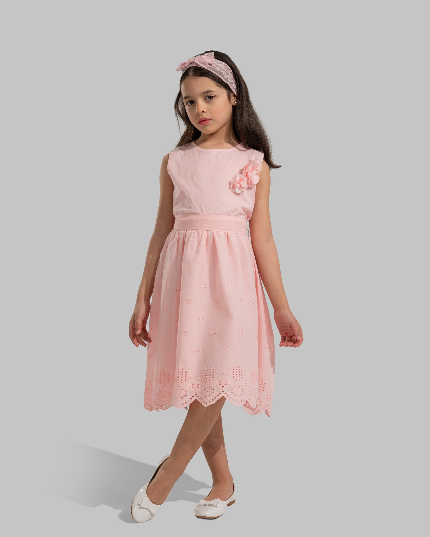 sleeveless pink cotton eyelet dress featuring a floral appliqué on the chest and a matching waist belt.